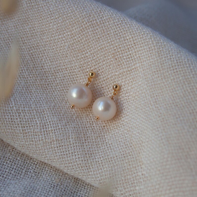 May include: A pair of gold stud earrings with white pearl accents.