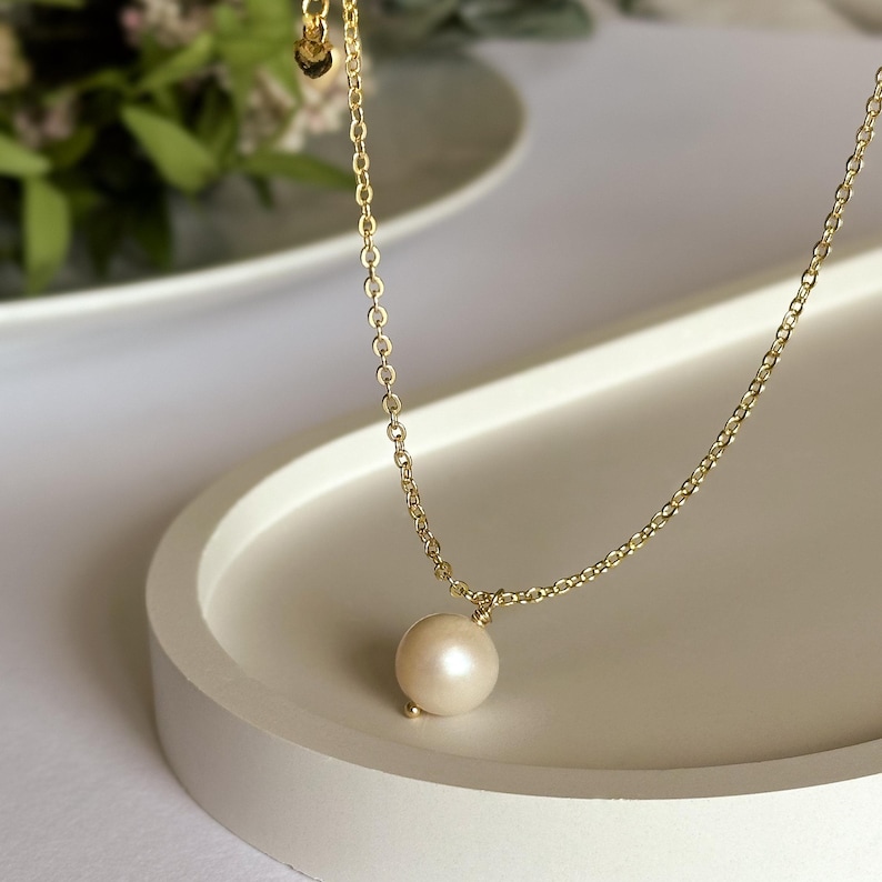 May include: A delicate gold chain necklace with a single, round, off-white pearl pendant.