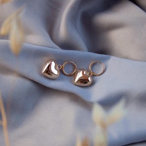 Puede incluir: Un par de pendientes de aro de coraz&oacute;n de oro. Los pendientes est&aacute;n hechos de un metal liso y brillante y tienen un dise&ntilde;o simple y elegante.
