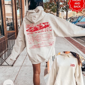 May include: Sand-colored hoodie with a red graphic of a race car and the text "#16 Leclerc" on the back. The front of the hoodie features the number "16" in red. The hoodie has a drawstring hood and a front pocket.