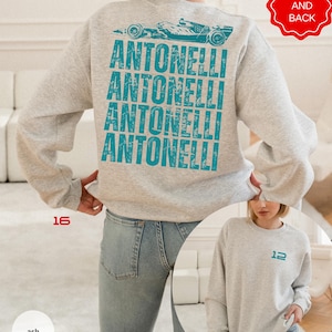 Pu&ograve; includere: Una felpa girocollo grigio cenere con una grafica color verde acqua di un'auto da corsa e il testo ANTONELLI ripetuto quattro volte sul retro. La parte anteriore della felpa mostra il numero 12 in verde acqua sul petto a sinistra.