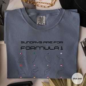 May include: Blue jean coloured t-shirt with the text "SUNDAYS ARE FOR FORMULA 1". The shirt features black outlines of race tracks with flags. The shirt is a Comfort Colors XL-TG-EG.