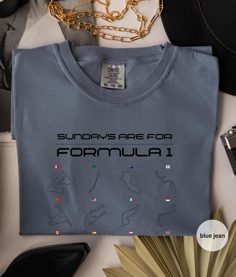 May include: Blue jean coloured t-shirt with the text "SUNDAYS ARE FOR FORMULA 1". The shirt features black outlines of race tracks with flags. The shirt is a Comfort Colors XL-TG-EG.