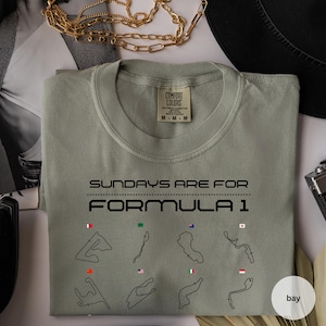 May include: Sage green Comfort Colors t-shirt with the text "SUNDAYS ARE FOR FORMULA 1" and race track illustrations. The shirt has a crew neck and a tag that reads "M-M-M".