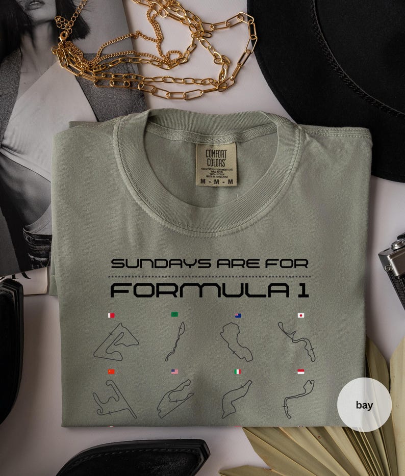 May include: Sage green Comfort Colors t-shirt with the text "SUNDAYS ARE FOR FORMULA 1" and race track illustrations. The shirt has a crew neck and a tag that reads "M-M-M".