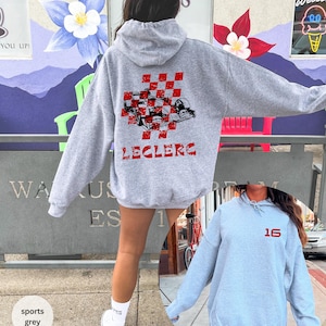 May include: Two grey hooded sweatshirts with red printed designs. One sweatshirt has a checkered flag and the word "Leclerc" printed on the back. The other sweatshirt has the number "16" printed on the front.