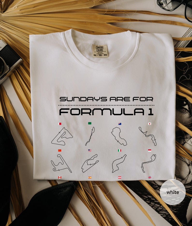May include: White crew neck sweatshirt with the text "SUNDAYS ARE FOR FORMULA 1" in black. Below the text are black outlines of race tracks with corresponding flags. The sweatshirt is a Comfort Colors brand.