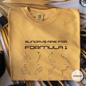 May include: Mustard-coloured t-shirt featuring the text "SUNDAYS ARE FOR FORMULA 1". Below the text are black line drawings of race tracks, each with a flag. The shirt is XL-TG-EG. The colour is described as mustard.