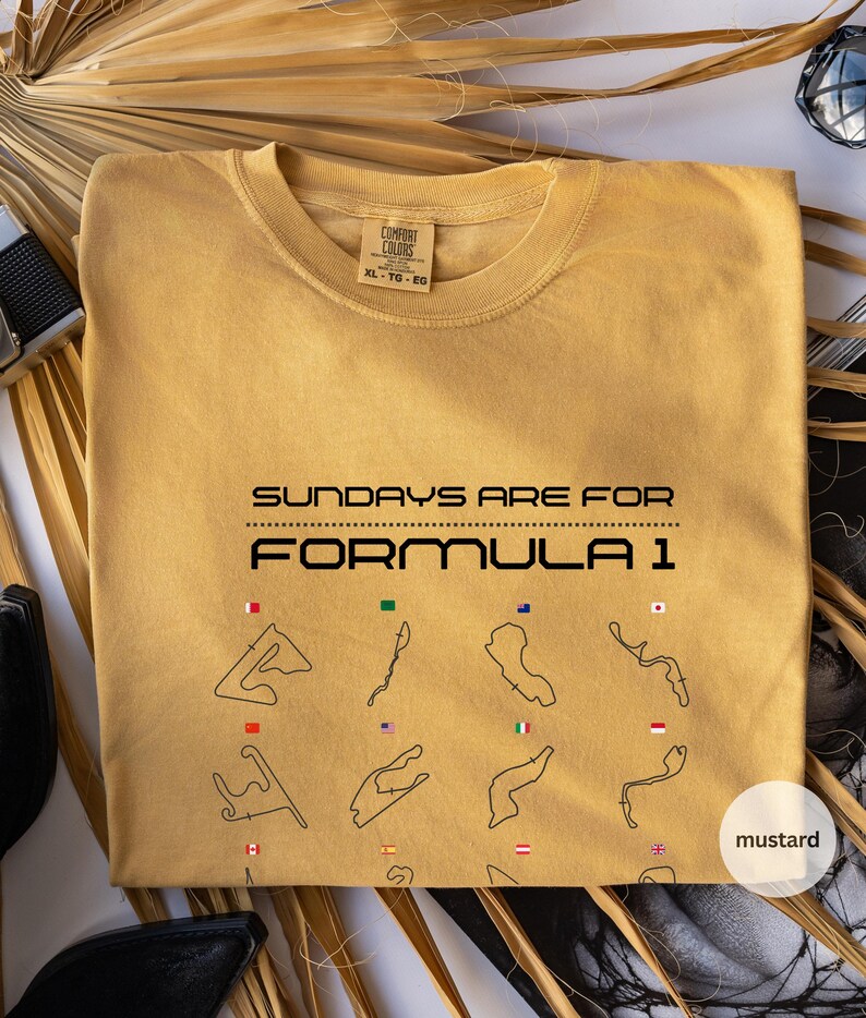 May include: Mustard-coloured t-shirt featuring the text "SUNDAYS ARE FOR FORMULA 1". Below the text are black line drawings of race tracks, each with a flag. The shirt is XL-TG-EG. The colour is described as mustard.