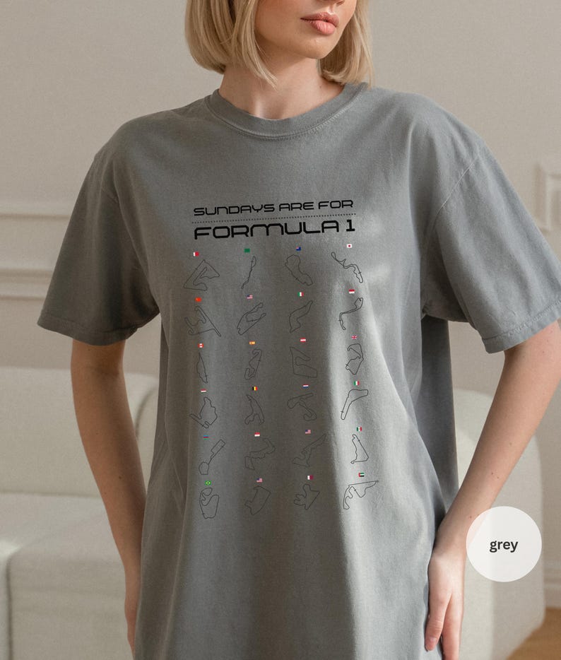 May include: Grey t-shirt featuring the text "SUNDAYS ARE FOR FORMULA 1" and a grid of race track outlines with flags. The shirt is a solid grey colour and has short sleeves.