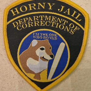 Puede incluir: Un parche bordado negro y amarillo con el texto "Horny Jail Department of Corrections" y un dibujo animado de Shiba Inu con el texto "I'm the one who bonks" debajo.