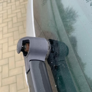 May include: Close-up of a black car windshield wiper arm with a gray plastic cover. The wiper arm is attached to the windshield and is in the down position.