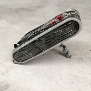 Puede incluir: Una multiherramienta plateada con mango negro y detalles rojos. La herramienta está plegada y tiene un sacacorchos en la parte inferior.