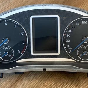 May include: A black car dashboard with three gauges. The gauges are for RPM, speed, and fuel level. The gauges have white needles and white numbers. The dashboard has a black and white carbon fiber pattern.