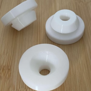 May include: Three white ceramic funnel-shaped objects with a small hole in the center. The objects are on a light brown wooden surface.