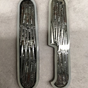 Puede incluir: Dos manillas de puerta de metal de color plateado con un borde blanco. Las manillas están decoradas con un patrón de líneas verticales.