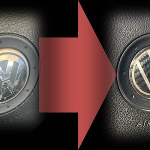 Op de afbeelding: Vergelijking van een Volkswagen stuurwiel embleem voor en na. Het linker embleem is beschadigd, het rechter heeft een koolstofvezel ontwerp. Het woord "AIRBAG" is rechts zichtbaar. Een rode pijl is aanwezig.