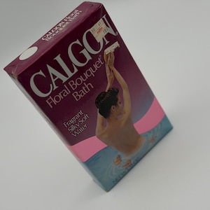 May include: A rectangular Calgon Floral Bouquet Bath product box in shades of deep purple, pink, and blue. The packaging features the brand name, the text Fragrant Silky Soft Water, and an illustration of a person bathing in water with flowers.