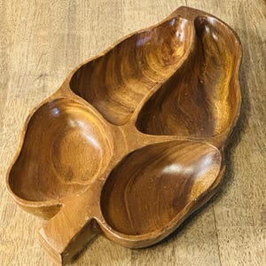 May include: A wooden serving tray with four pear-shaped compartments. The tray is made of light brown wood with a natural grain pattern. The tray is designed to hold snacks or appetizers.
