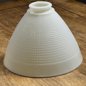May include: A white, cone-shaped glass lampshade with a textured, grid-like pattern. The lampshade has a smooth, rounded base and a cylindrical top opening. The shade is designed to diffuse light.