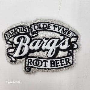 Può includere: Toppa ricamata con il logo Barg's Root Beer. La toppa ha uno sfondo nero, scritte bianche e un bordo argentato. Il testo include "FAMOUS OLDE TYME" e "ROOT BEER".