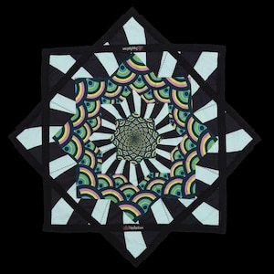 May include: A square fabric wall hanging featuring a central star-shaped pattern with concentric rainbow-colored arches in pink, yellow, blue, and green. The design radiates outward with black and light blue stripes, finished with a black border.
