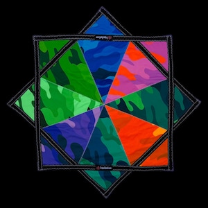 May include: A colorful, geometric quilt with a camouflage pattern in shades of green, blue, purple, orange, and pink. The quilt is stitched together with black thread and has the text "TrippySquad.com" on the edges. The quilt is set against a black background.