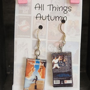 May include: A pair of earrings featuring miniature VHS tapes of the movie "The Karate Kid". One earring features the front cover of the VHS tape, while the other earring features the back cover. The earrings are handmade and are available for purchase from the shop "All Things Autumn".