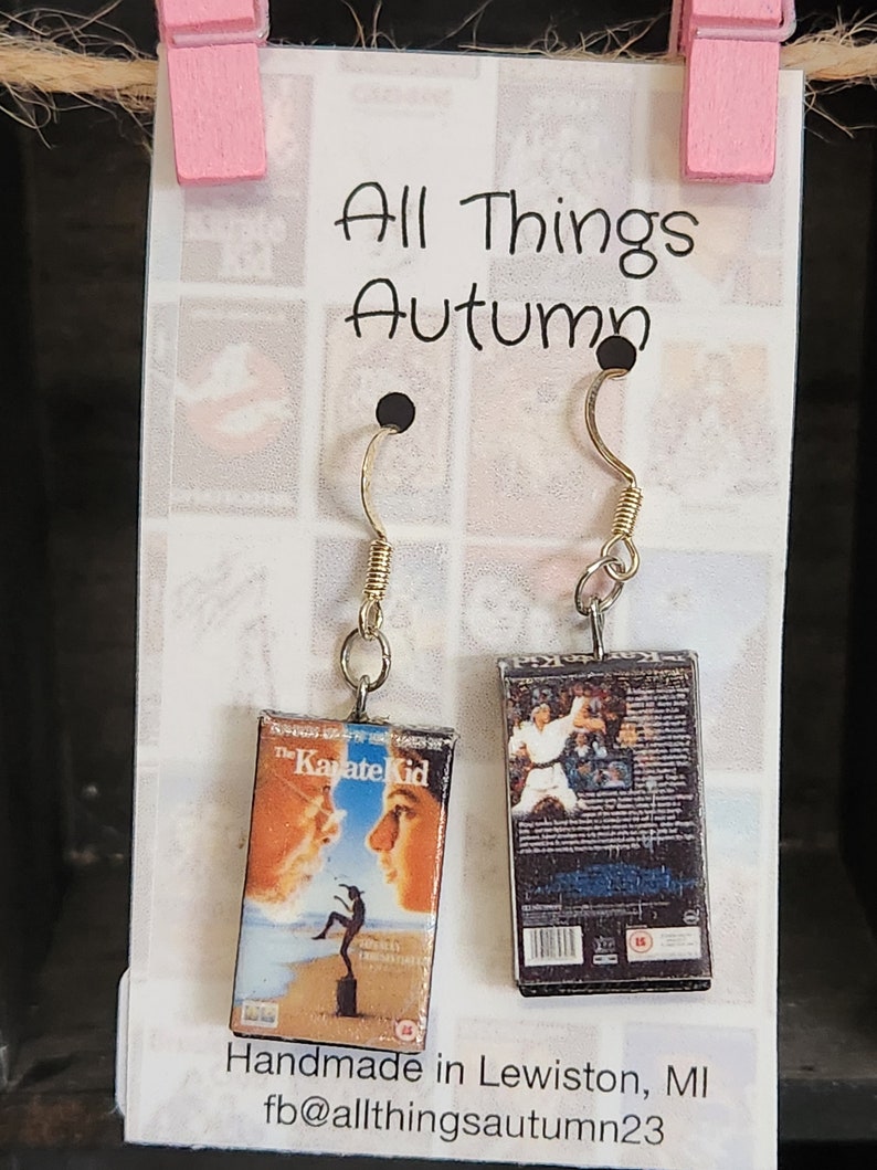 May include: A pair of earrings featuring miniature VHS tapes of the movie "The Karate Kid". One earring features the front cover of the VHS tape, while the other earring features the back cover. The earrings are handmade and are available for purchase from the shop "All Things Autumn".