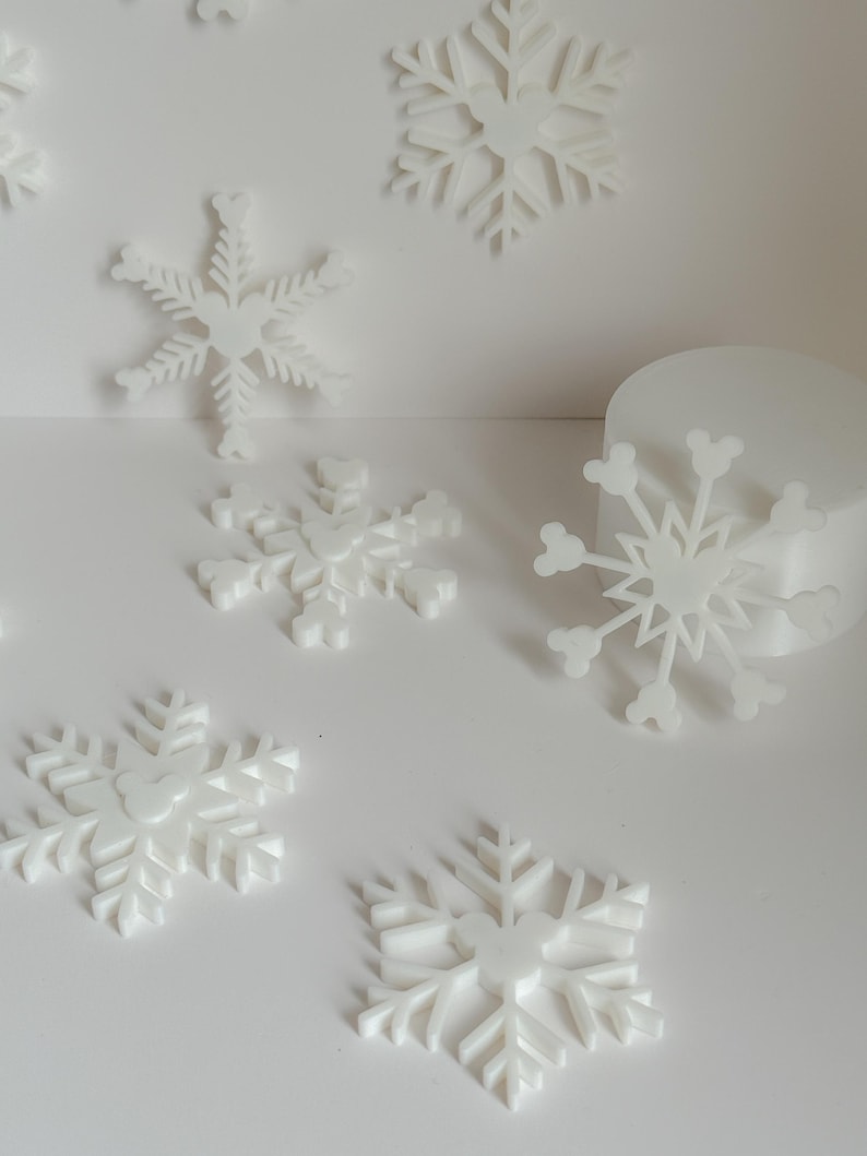 May include: White snowflake decorations in various sizes and designs. The snowflakes have a three-dimensional appearance and are scattered across a white surface. The image is well-lit, highlighting the intricate details of each snowflake, perfect for winter-themed crafts and decor.