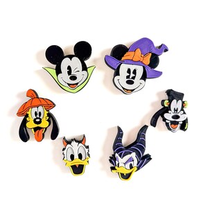 Può includere: Un set di sei ciondoli per scarpe raffiguranti vari personaggi in costumi a tema Halloween, tra cui un vampiro, una strega, una zucca, un mostro, un diavolo e un cattivo con le corna, realizzati in plastica vivace e resistente.