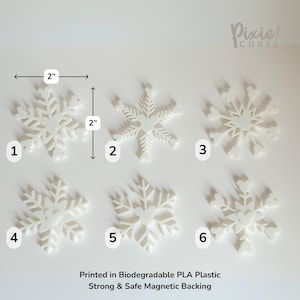 May include: Six white snowflake-shaped ornaments, each approximately 2 inches in diameter, are displayed on a white surface. The ornaments are numbered 1 through 6. The text "Printed in Biodegradable PLA Plastic Strong & Safe Magnetic Backing" is visible.