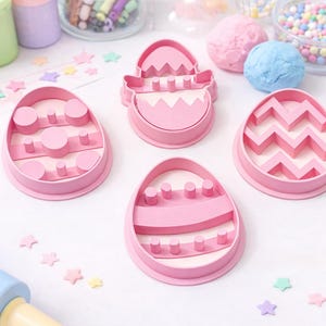 Puede incluir: Cortadores de galletas rosas con forma de huevo de Pascua con varios diseños. La imagen también muestra chispas de colores, plastilina y confeti en forma de estrella, lo que sugiere un tema de repostería o manualidades.