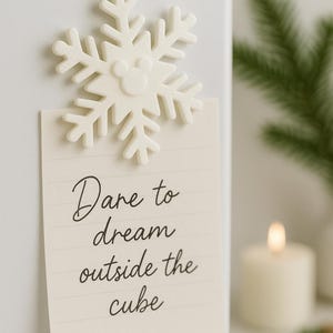 May include: A white snowflake-shaped magnet with a Mickey Mouse silhouette in the center, attached to a cream-colored notepad. The notepad has the words "Dare to dream outside the cube" written on it in cursive.