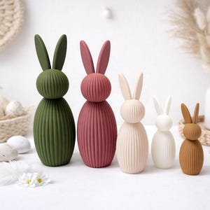 Pu&ograve; includere: Una collezione di figurine decorative a forma di coniglietti pasquali in varie dimensioni e colori. I coniglietti sono in tonalit&agrave; di verde, malva, crema, bianco e marrone. Ogni coniglietto ha un corpo a coste e lunghe orecchie.
