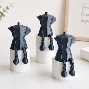 May include: Three dark gray moka pot figurines with articulated legs and feet, each perched on a white cylindrical base. The moka pots feature a classic octagonal shape with a handle and spout, designed with jointed limbs that hang over the edge.