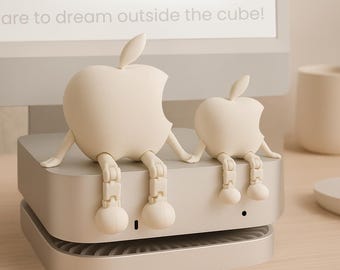 May include: Two off-white apple-shaped figurines with articulated legs are perched on a silver computer device. The text "Pixie! CUBE" is visible on the screen behind them, along with the phrase "are to dream outside the cube!"