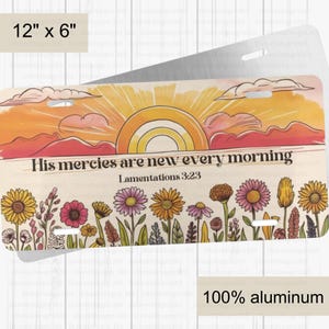May include: A 12" x 6" aluminum license plate with a watercolor sunset scene and wildflowers. The text "His mercies are new every morning" is printed in black with the scripture reference "Lamentations 3:23" below. The plate is made of 100% aluminum.