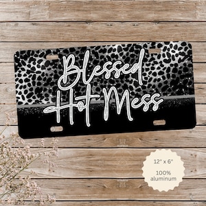 May include: A black and white license plate with the words "Blessed Hot Mess" in white script. The top half features a black and white animal print, and the bottom half is solid black. The plate measures 12" x 6".
