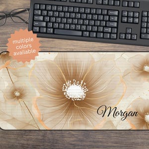 May include: A rectangular mouse pad featuring a floral design in shades of beige and gold. The design includes large, stylized flowers with delicate lines and a white center. The name "Morgan" is written in cursive. The text "multiple colors available" is also visible.