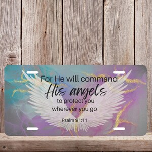 May include: A purple and blue watercolor background with gold glitter accents. White angel wings with a black text overlay that reads "For He will command His angels to protect you wherever you go Psalm 91:11".