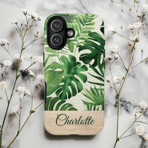 May include: A phone case featuring a vibrant green tropical leaf pattern on a white background. The bottom section has a wood-grain appearance with the name "Charlotte" in a cursive font. The case is designed for a smartphone.
