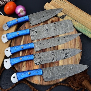May include: Five blue-handled kitchen knives with a Damascus steel blade pattern. The knives are arranged on a wooden cutting board.