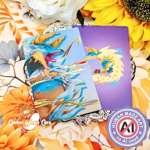 May include: Two fantasy art cards with dragon illustrations. One card has a blue background with a detailed dragon, the other a purple background with a geometric dragon. The cards are on a decorative silver tray, surrounded by flowers.