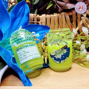 Puede incluir: Dos llaveros en miniatura de bebida energética verde lima. Uno presenta una etiqueta de información nutricional, el otro muestra el texto "Best Served Cold" y "Spite Energy Drink". Ambos están diseñados para parecer pequeñas latas de refresco.