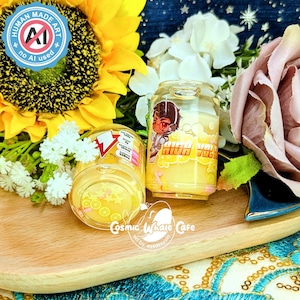 May include: Two clear, cylindrical containers with yellow liquid and cartoon graphics. One container has a red and yellow lightning bolt design, the other has a cartoon character and the words "HIGH VOLT". The containers sit on a wooden tray with flowers.