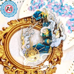May include: A clear acrylic charm featuring a stylized illustration of a mechanical figure with blue and gold accents, lightning bolts, and a sun-like wheel. The charm is set against a gold-colored ornate frame. Text on the charm reads "HUMAN MADE ART" and "no AI used".