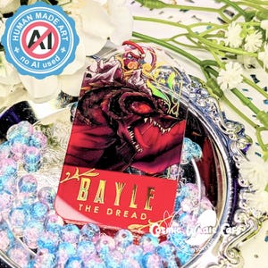 May include: A clear acrylic tag featuring a red and black illustration of a dragon with the text "BAYLE THE DREAD" on a red background. The tag is on a silver tray with blue and pink beads. A blue and white badge reads "HUMAN MADE ART, no AI used."