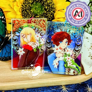 May include: Two acrylic charms featuring anime-style characters with floral bouquets. One charm has a blonde character in a dark jacket, the other has a red-haired character in a blue jacket. The charms have a holographic effect and the text "FALCON" and "Cosmic Whale Cafe" are visible.