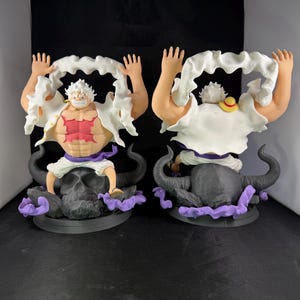 May include: Two white and red anime figurines of a character with white hair and a white beard. The figurines are posed with their arms raised and are wearing white clothing. The figurines are sitting on black bull skulls with purple smoke.